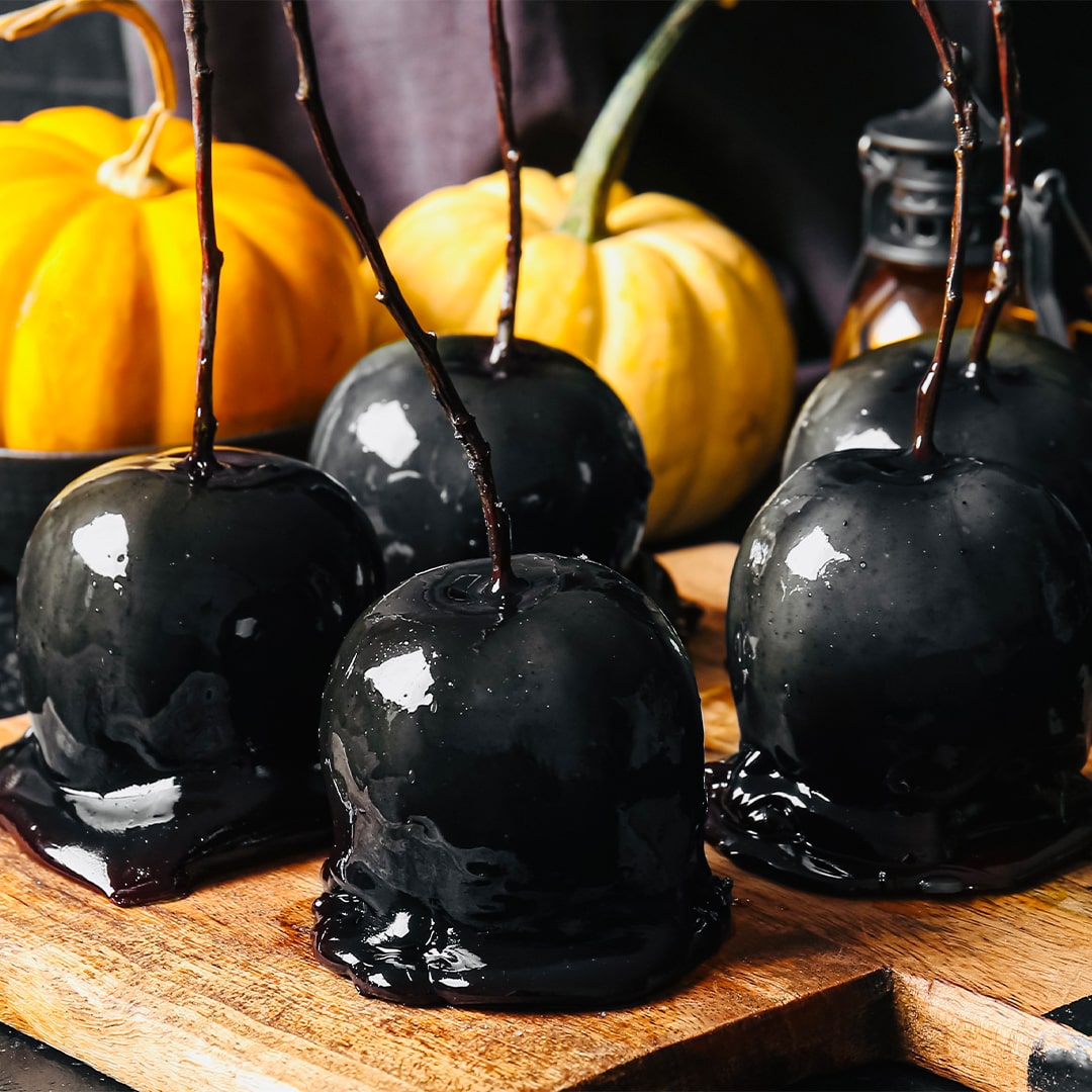 Black candy apples on a wooden board with pumpkins in the background