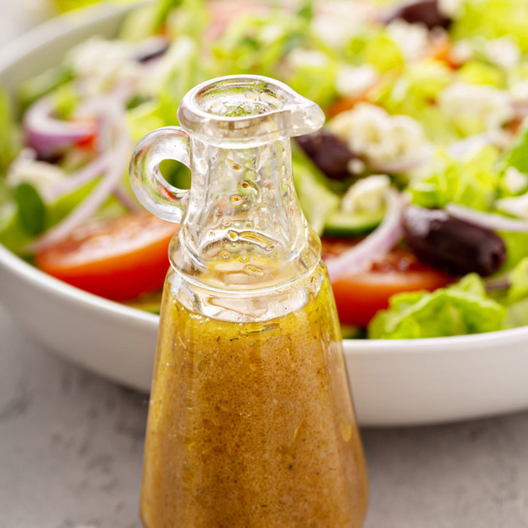 Glass bottle of salad dressing with a salad in the background