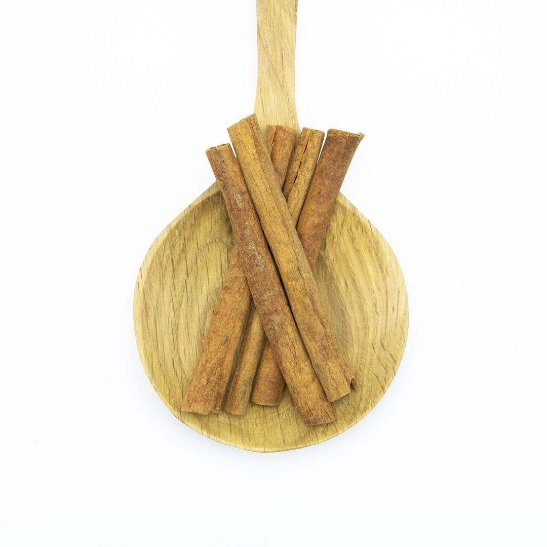 A wooden spoon holding several cinnamon sticks against a white background.