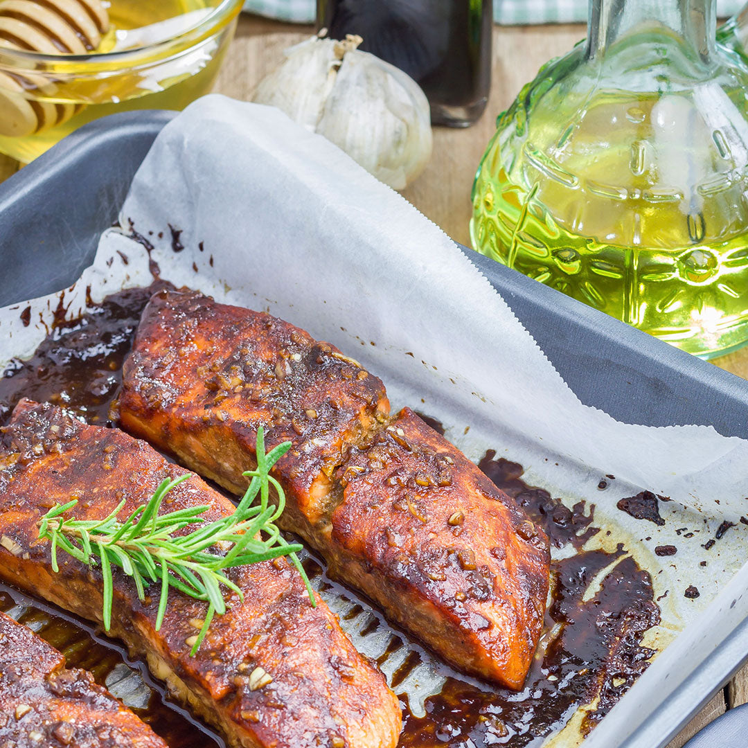 Baked salmon fillets with a sprig of rosemary on a baking tray, surrounded by cooking ingredients.