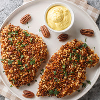 Two pieces of breaded chicken with a side of mustard on a white plate.
