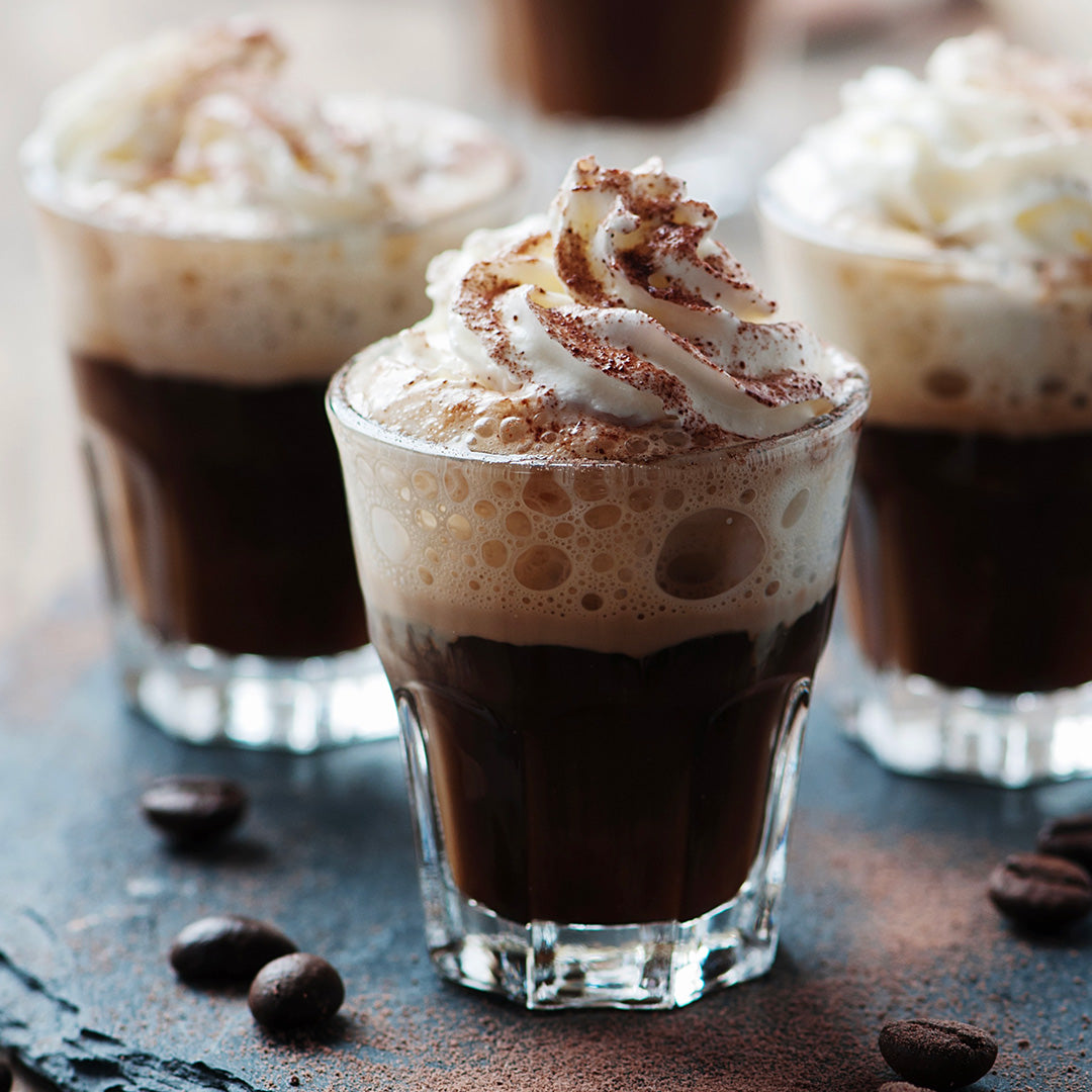 Three shot glasses filled with a layered drink topped with whipped cream on a dark surface.
