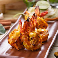 Grilled tandoori shrimp skewers on a wooden plate with a blurred background
