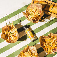 Baskets of fries with a seasoning bottle on a green and white striped surface