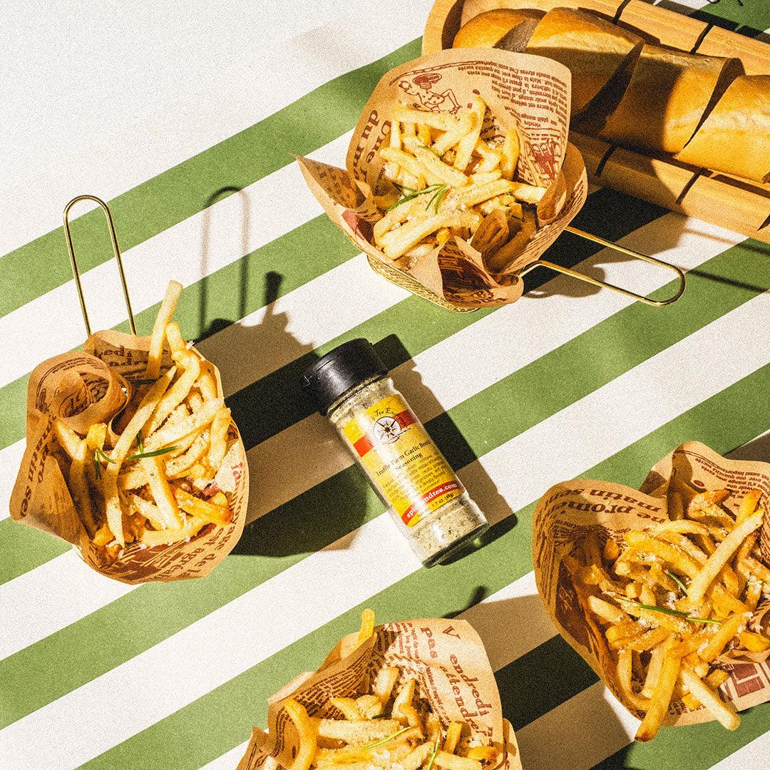 Baskets of fries with a seasoning bottle on a green and white striped surface